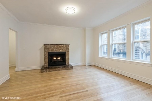 unfurnished living room with light wood-type flooring, crown molding, baseboards, and a premium fireplace