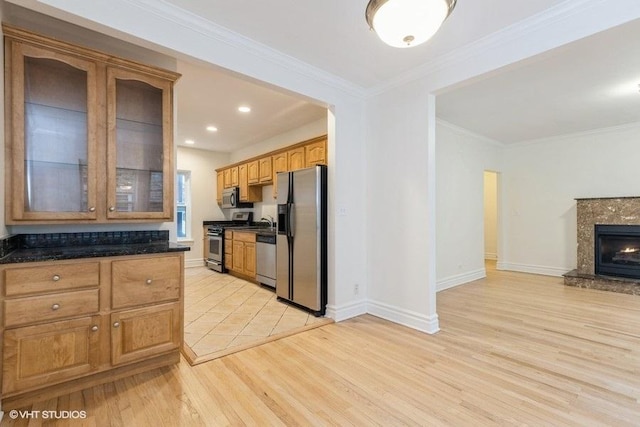 kitchen featuring crown molding, stainless steel appliances, light wood-style flooring, a premium fireplace, and glass insert cabinets