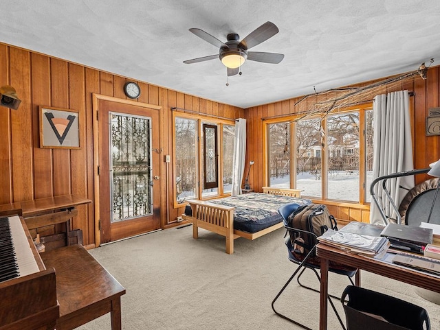 carpeted bedroom with ceiling fan, access to exterior, and wooden walls