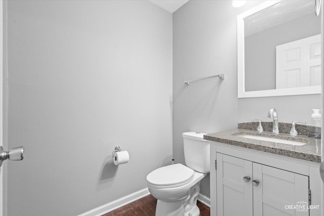 half bath featuring baseboards, vanity, toilet, and wood finished floors