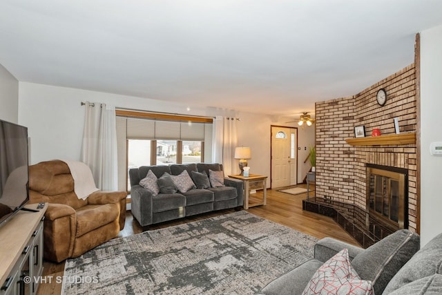 living room with light wood finished floors, ceiling fan, and a brick fireplace