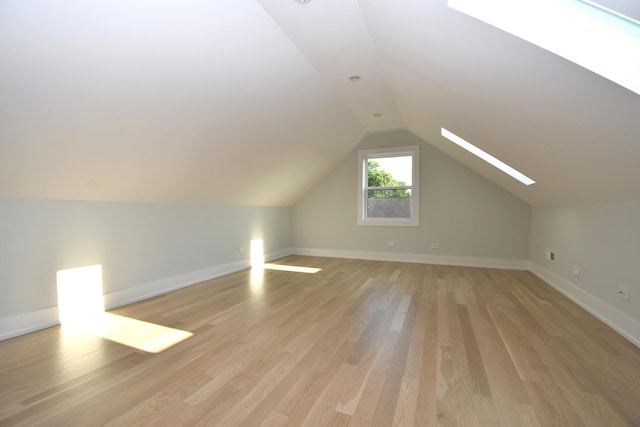 additional living space featuring lofted ceiling with skylight and light hardwood / wood-style flooring