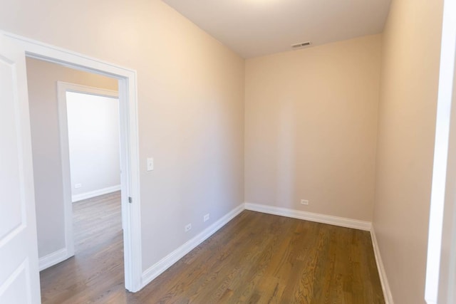 empty room featuring dark wood-type flooring, visible vents, and baseboards