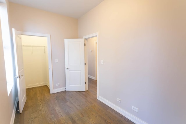 unfurnished bedroom featuring a closet, a spacious closet, baseboards, and wood finished floors