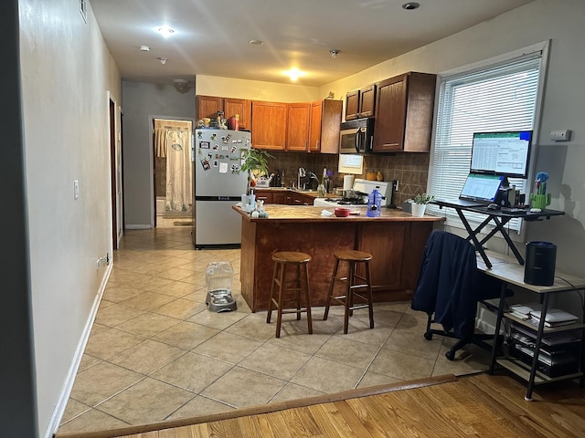 kitchen featuring light tile patterned floors, a breakfast bar, appliances with stainless steel finishes, tasteful backsplash, and kitchen peninsula
