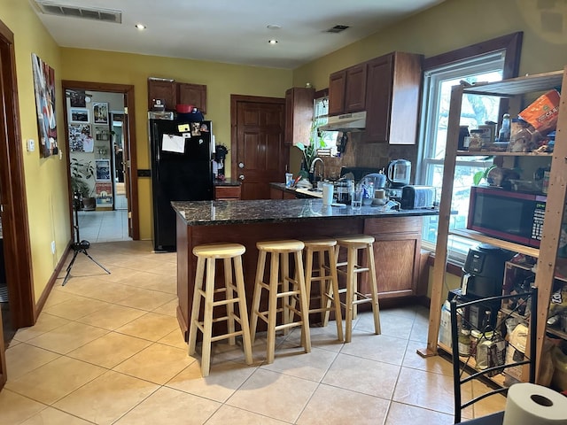 kitchen featuring light tile patterned flooring, a kitchen bar, black fridge, tasteful backsplash, and kitchen peninsula