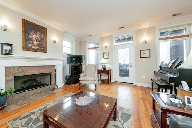 living room featuring light wood-style flooring, a premium fireplace, visible vents, and crown molding