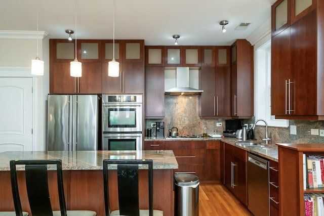 kitchen featuring decorative backsplash, wall chimney exhaust hood, appliances with stainless steel finishes, light stone countertops, and a sink