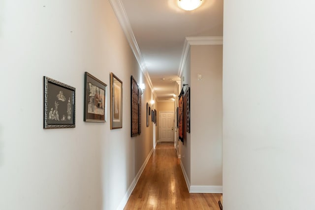 corridor featuring baseboards, ornamental molding, and light wood-style floors