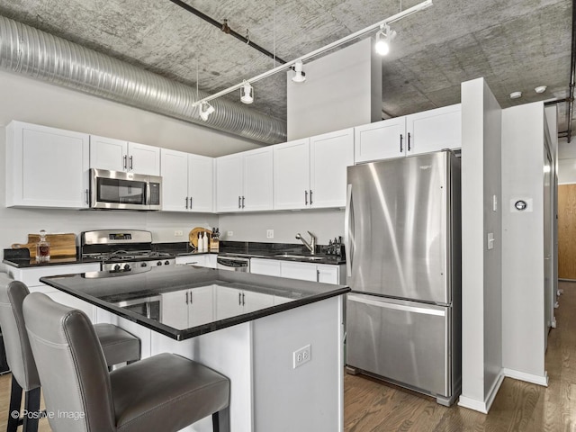 kitchen featuring dark countertops, appliances with stainless steel finishes, white cabinetry, a kitchen island, and a kitchen bar