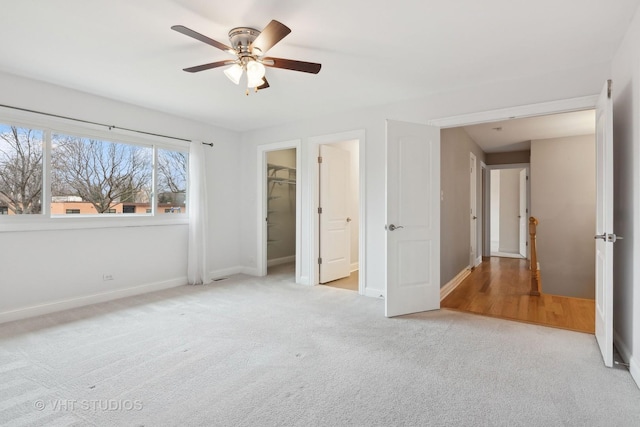 unfurnished bedroom with light carpet, a walk in closet, a closet, and ceiling fan