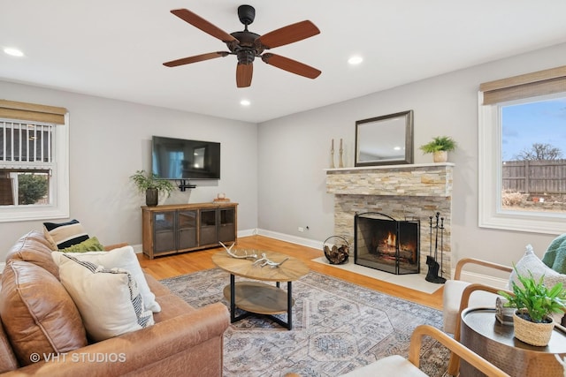 living room featuring ceiling fan, a stone fireplace, and light wood-type flooring