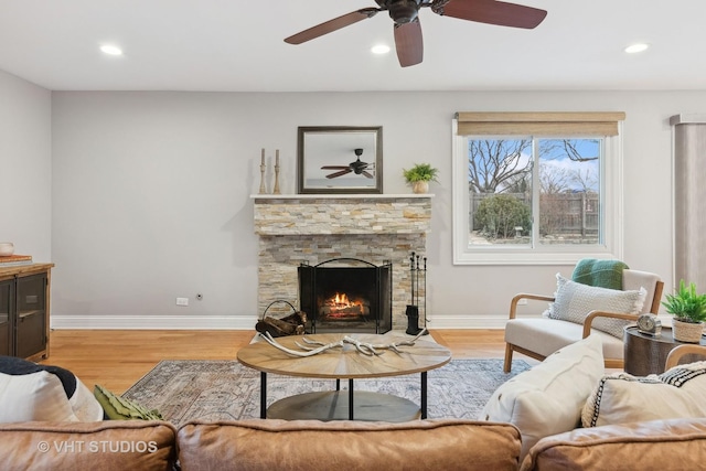 living room featuring ceiling fan, a stone fireplace, and light hardwood / wood-style flooring