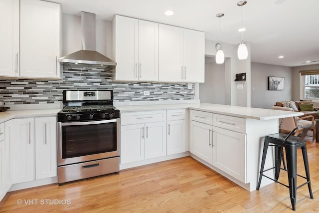 kitchen with white cabinets, stainless steel range with gas stovetop, kitchen peninsula, and wall chimney range hood