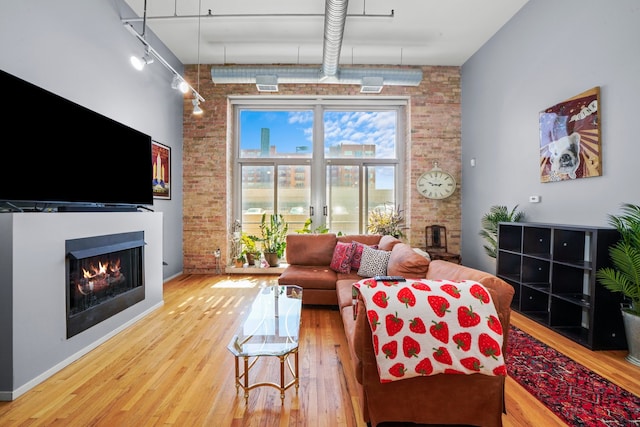 living room featuring brick wall, rail lighting, and hardwood / wood-style floors