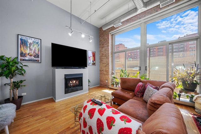 living room featuring a high ceiling, wood-type flooring, rail lighting, and brick wall