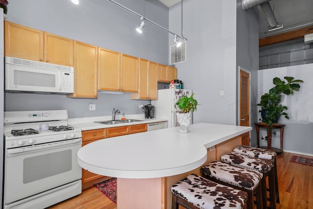 kitchen with sink, white appliances, a breakfast bar area, a towering ceiling, and decorative light fixtures