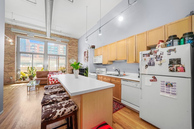 kitchen featuring sink, light wood-type flooring, a kitchen bar, track lighting, and white appliances