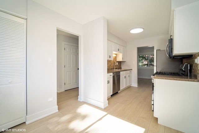 kitchen featuring backsplash, appliances with stainless steel finishes, light hardwood / wood-style floors, and white cabinets