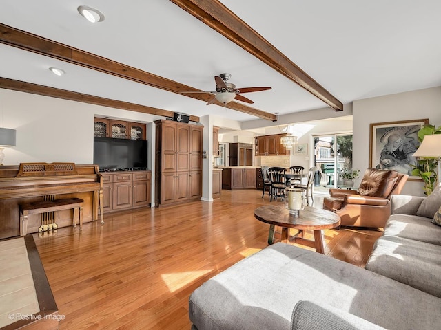 living area with a ceiling fan, light wood-type flooring, and beam ceiling