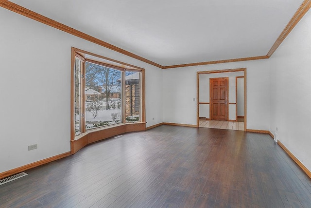 empty room with baseboards, wood finished floors, visible vents, and crown molding