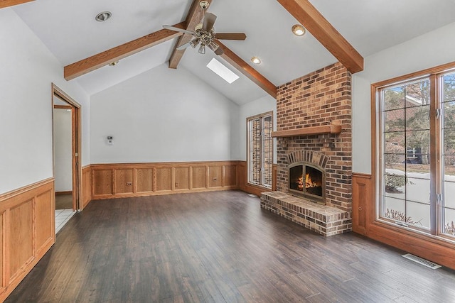 unfurnished living room featuring ceiling fan, dark wood-type flooring, a fireplace, and vaulted ceiling with skylight