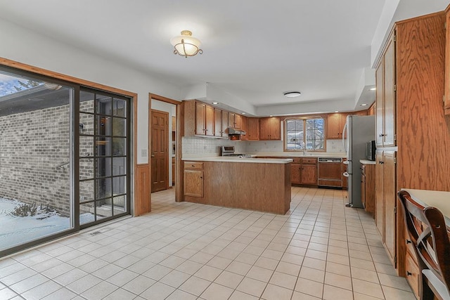 kitchen with light tile patterned flooring, light countertops, freestanding refrigerator, brown cabinets, and dishwasher