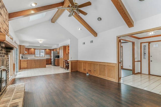 unfurnished living room with a brick fireplace, light hardwood / wood-style flooring, lofted ceiling with skylight, and ceiling fan