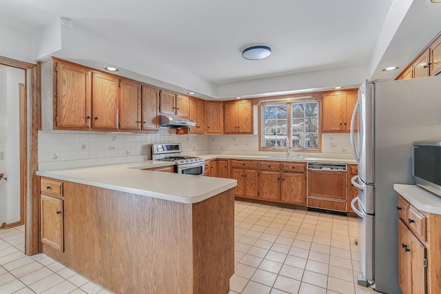 kitchen with under cabinet range hood, stainless steel appliances, a peninsula, a sink, and light countertops