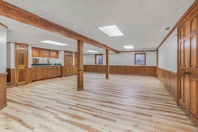 basement with a paneled ceiling, light hardwood / wood-style floors, and wood walls