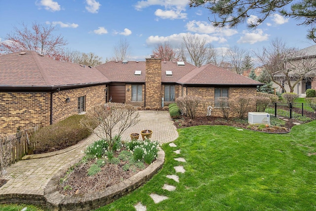 back of property featuring brick siding, a shingled roof, fence, a yard, and a chimney