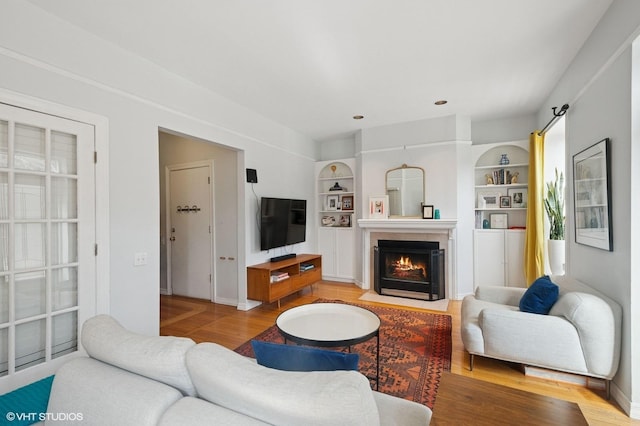 living area with a fireplace with flush hearth, built in features, baseboards, and wood finished floors