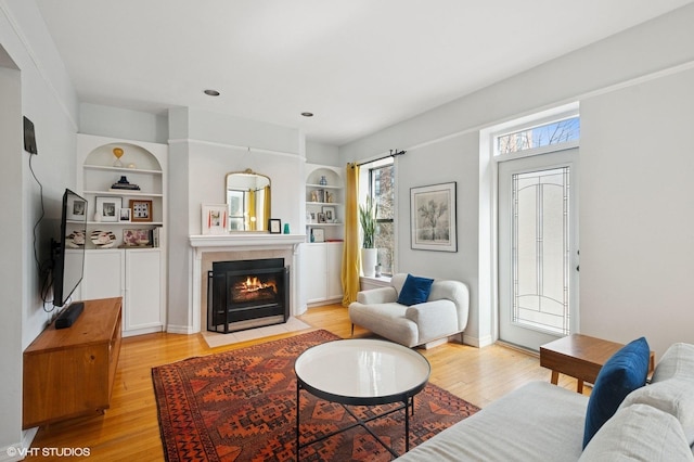 living room featuring built in shelves, light wood-style floors, and a fireplace with flush hearth