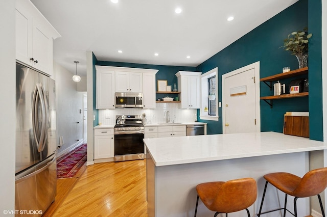 kitchen featuring open shelves, a peninsula, white cabinets, stainless steel appliances, and a sink