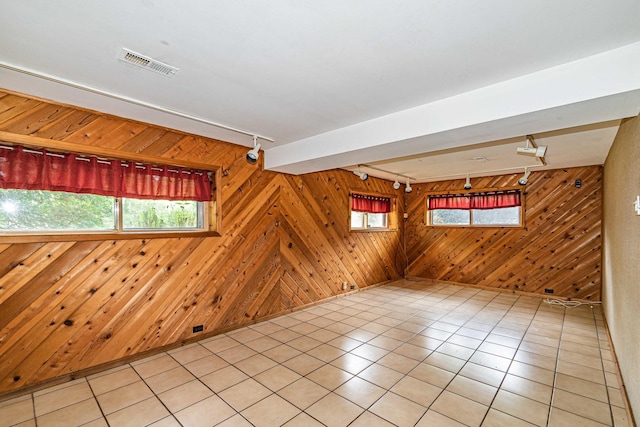 unfurnished room featuring plenty of natural light, track lighting, wooden walls, and light tile patterned floors