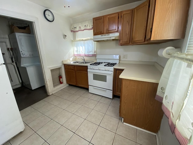 kitchen with stacked washer and dryer, sink, light tile patterned floors, and white gas range oven