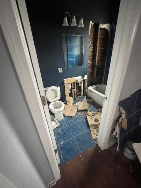 bathroom with a tub to relax in, tile patterned floors, and toilet