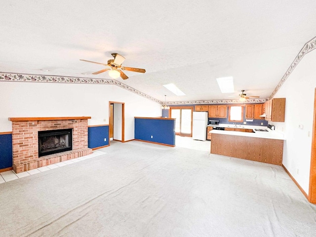 interior space with vaulted ceiling with skylight, a textured ceiling, a fireplace, white fridge, and light colored carpet