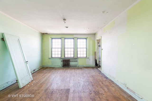 empty room with crown molding, wood-type flooring, and radiator