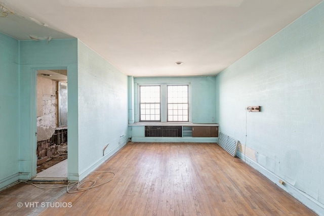 spare room featuring wood-type flooring, brick wall, and radiator