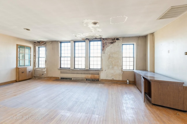 spare room featuring a healthy amount of sunlight, radiator heating unit, and light wood-type flooring