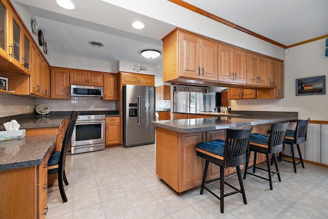 kitchen featuring crown molding, stainless steel appliances, tasteful backsplash, a kitchen bar, and kitchen peninsula