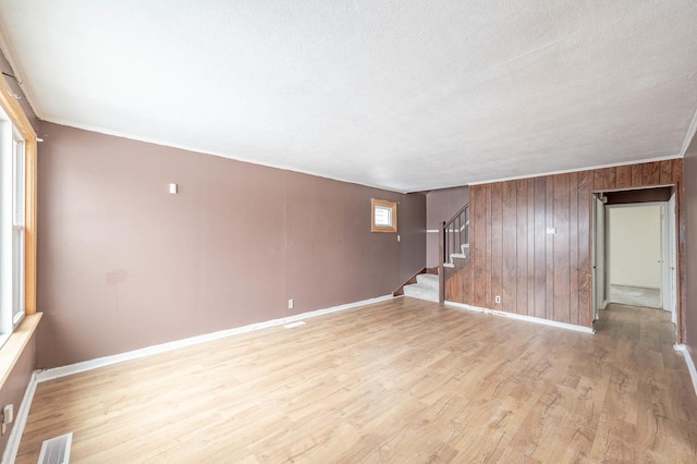 empty room featuring crown molding, wooden walls, a textured ceiling, and light hardwood / wood-style floors