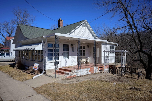 view of front facade featuring covered porch, a shingled roof, and a chimney