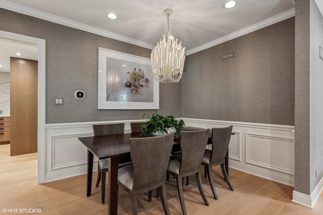 dining area with light wood-style floors, ornamental molding, and an inviting chandelier