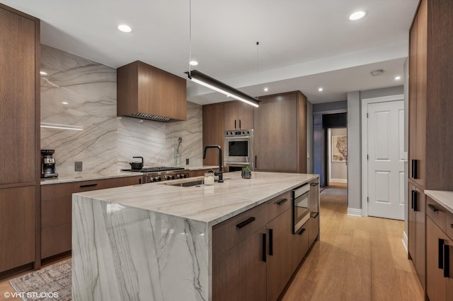 kitchen with a spacious island, light wood-style flooring, appliances with stainless steel finishes, light stone counters, and a sink