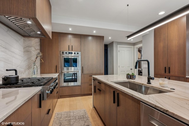 kitchen with stainless steel appliances, exhaust hood, a sink, light wood-style floors, and backsplash