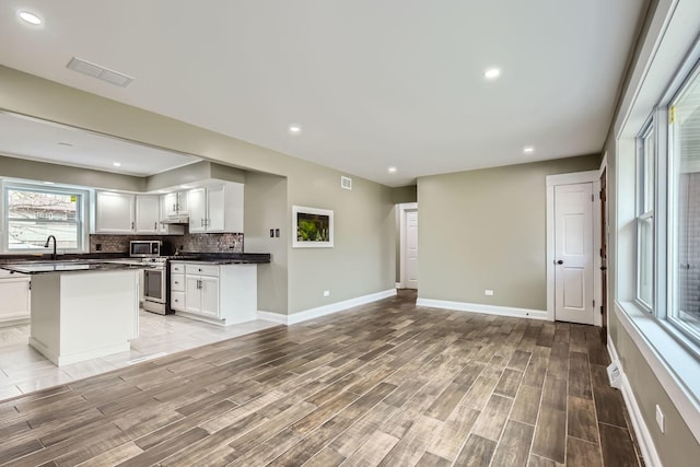 kitchen featuring a center island, light wood-type flooring, white cabinets, stainless steel appliances, and backsplash