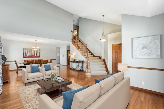 living area featuring high vaulted ceiling, light wood-style flooring, baseboards, and stairs