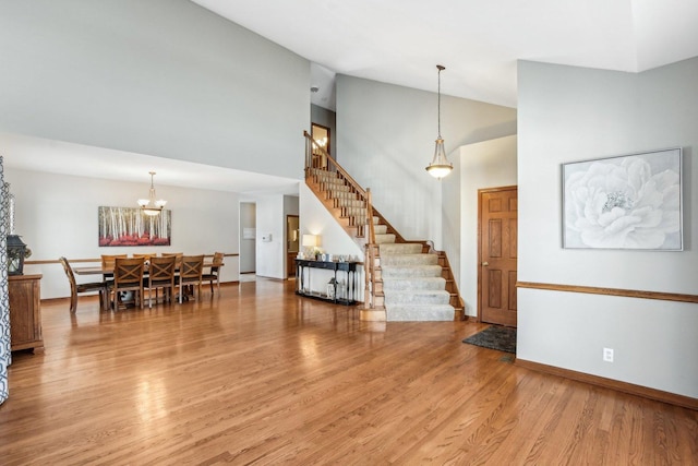 living room featuring stairway, an inviting chandelier, wood finished floors, high vaulted ceiling, and baseboards